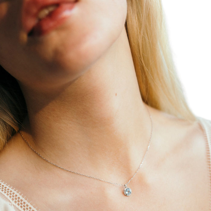 Modelo feminina a usar colar Lecarré em ouro branco, com topázio azul redondo e diamantes ao redor.