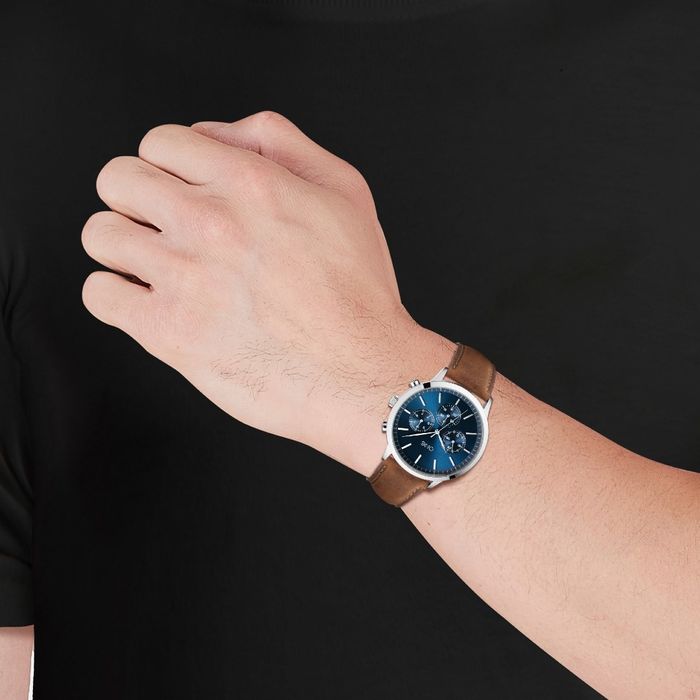 Modelo com um relógio masculino One de bracelete castanha e um mostrador azul estilo cronógrafo.