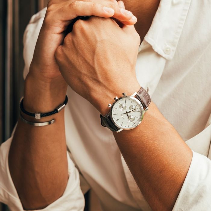 Modelo masculino com um relógio One, bracelete em pele e com um mostrador branco estilo cronógrafo.