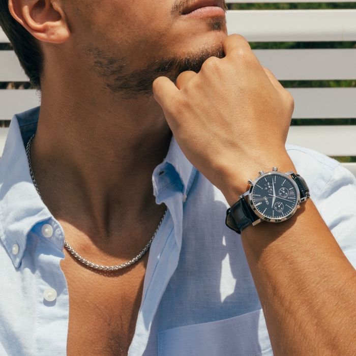 Modelo masculino com um relógio One de bracelete em pele e com um mostrador preto estilo cronógrafo.