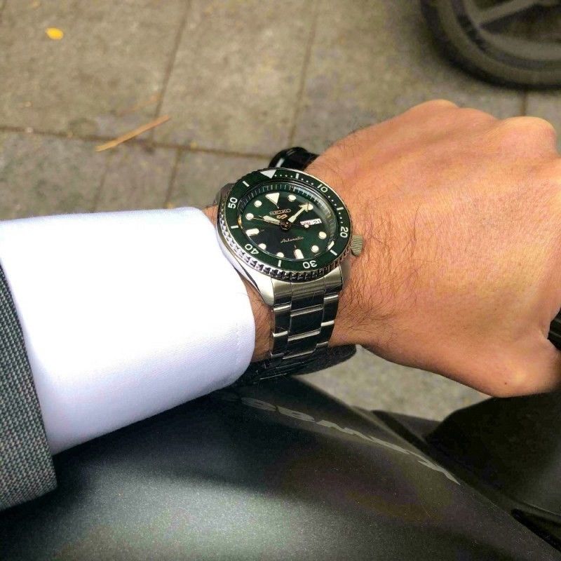 Pulso masculino com relógio Seiko 5 de bracelete e caixa em aço prateada, com mostrador verde.