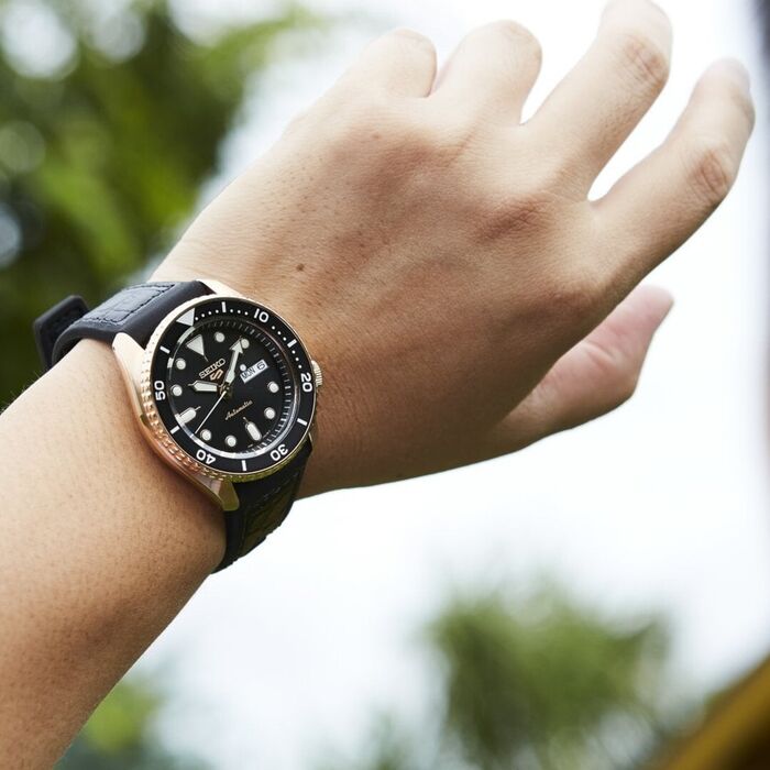 Imagem de pulso masculino com Seiko 5, bracelete silicone preta e caixa rose gold, mostrador preto.