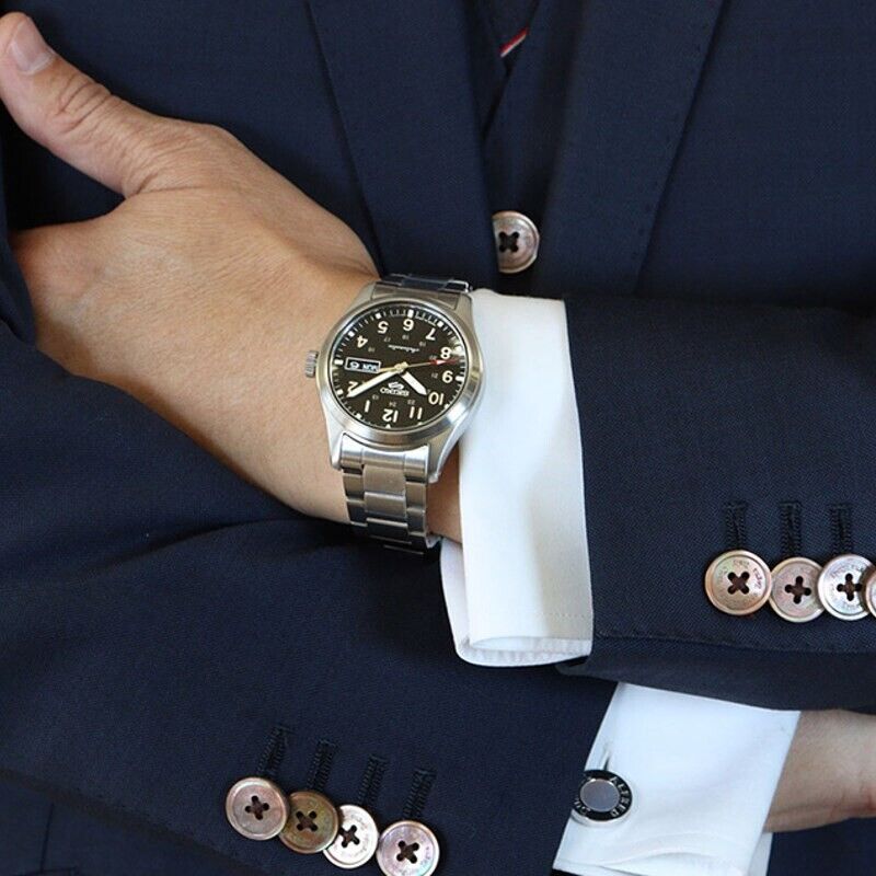 Pulso masculino com relógio Seiko 5, com bracelete e caixa em aço de cor prateada e mostrador preto.