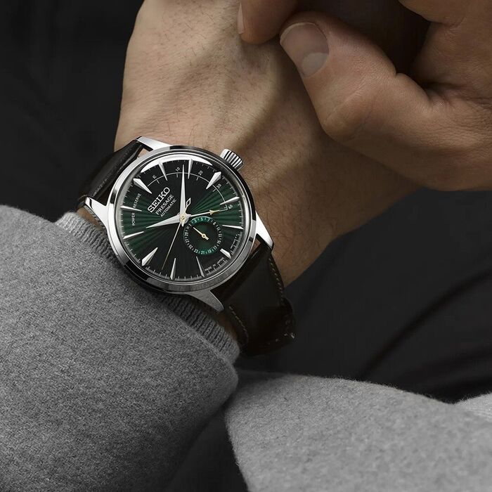 Pulso masculino com relógio Seiko Presage, bracelete em pele castanha e mostrador verde, clássico.