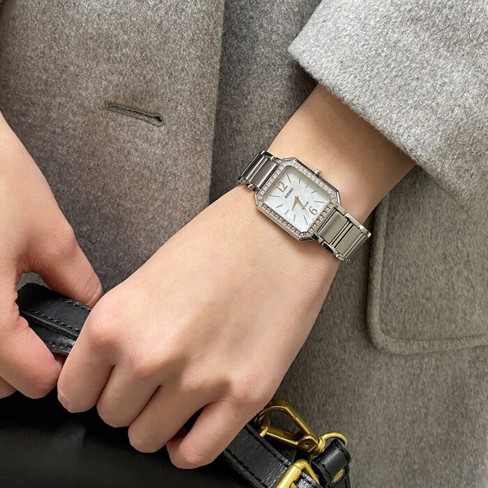 Pulso feminino com Seiko de bracelete e caixa prateada, mostrador retangular madrepérola e pedras.