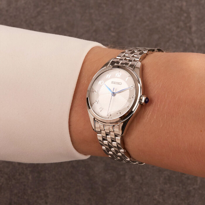 Pulso feminino com relógio Seiko feminino de bracelete e caixa prateada e com mostrador redondo.