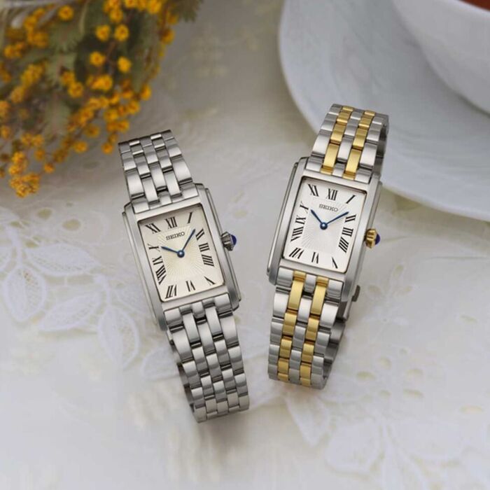 Vista de dois relógios Seiko feminino com caixa e bracelete prateada e mostrador retangular.
