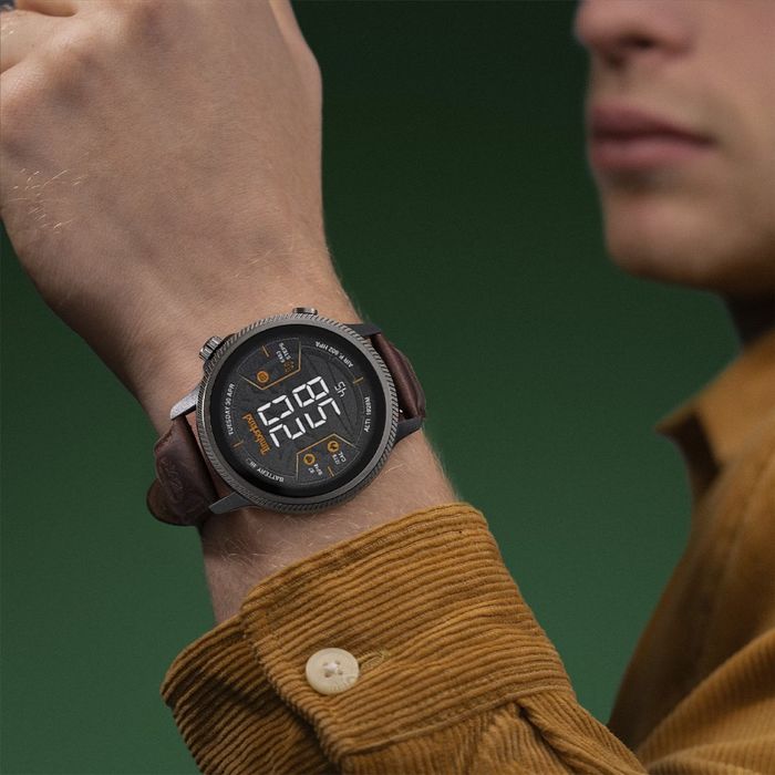 Modelo masculino com um Smartwatch da Timberland de bracelete em pele castanha sobre um fundo verde.