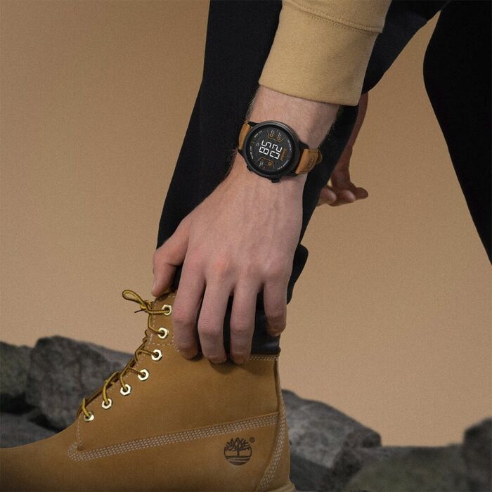 Modelo masculino com umas botas bege e um Smartwatch da Timberland de bracelete em pele bege.