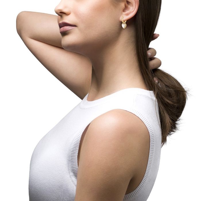 Modelo feminino com uma argola dourada Unike com pendente em coração com pedras e uma madrepérola.