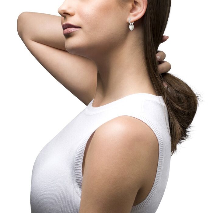 Modelo feminino com uma argola prateada Unike com pendente em coração com pedras e uma madrepérola.