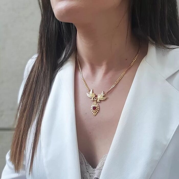 Modelo com um colar dourado Portugal Jewels com duas pombas, pedras rosas e um pendente de viana.