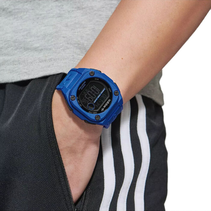 Relógio digital da Adidas azul em silicone no pulso de uma modelo feminina com a mão no bolso.