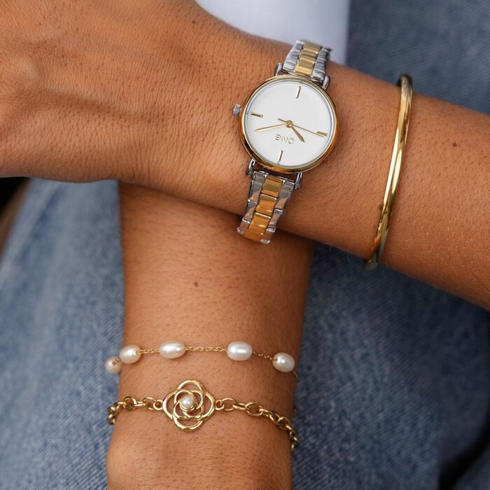 Braços femininos com relógio bicolor prateado e dourado e pulseiras e escrava douradas