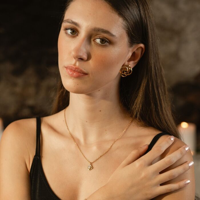 Senhora com colar dourado com pendente formato de botão de rosa recortada e pérola branca no centro
