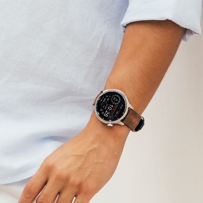 Modelo masculino com smartwatch ONE de mostrador redondo prateado e bracelete pele castanha.