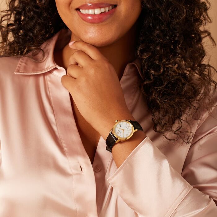Senhora com relógio Citizen com bracelete em pele preta, caixa dourada e mostrador redondo branco