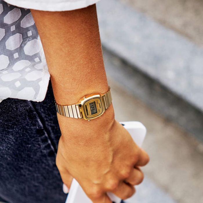Modelo com um relógio Casio em aço dourado de pequenas dimensões e com um mostrador digital.