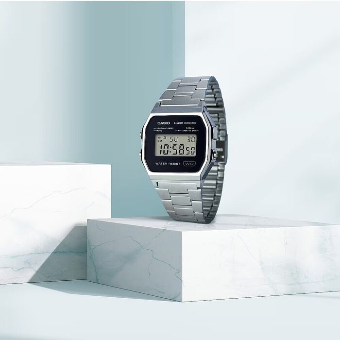 Relógio digital prateado com bracelete metálica e mostrador retangular preto.