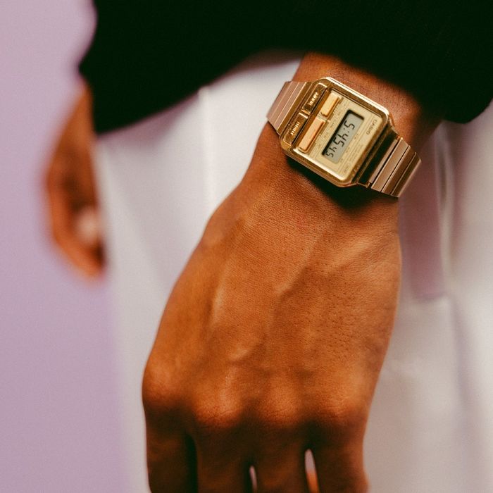 Relógio digital dourado com mostrador retangular e pulseira metálica no pulso.