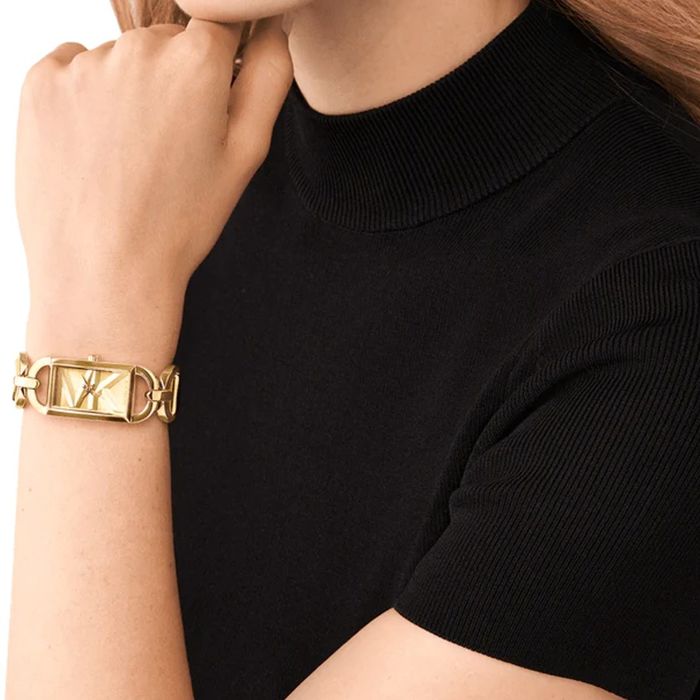 Relógio Michael Kors para mulher com aço inoxidável dourado com formato rectângular, no pulso.