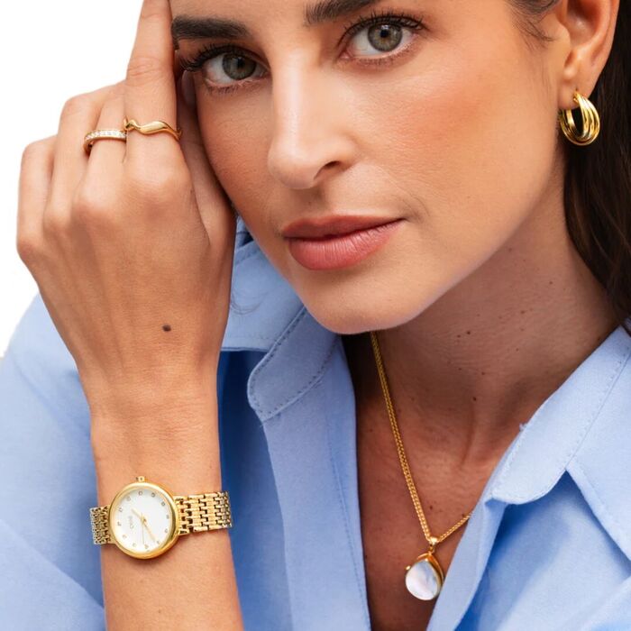 Modelo com um colar e um relógio One dourado de mostrador com pedras e um coração no índice das 9h.
