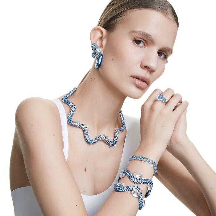Anel Swarovski feminino aberto com dois cristais azuis de duas medidas diferentes, no dedo da modelo.