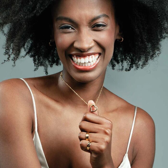 Modelo feminino com um colar dourado One de malha fina e com um pendente de um coração com pedras.