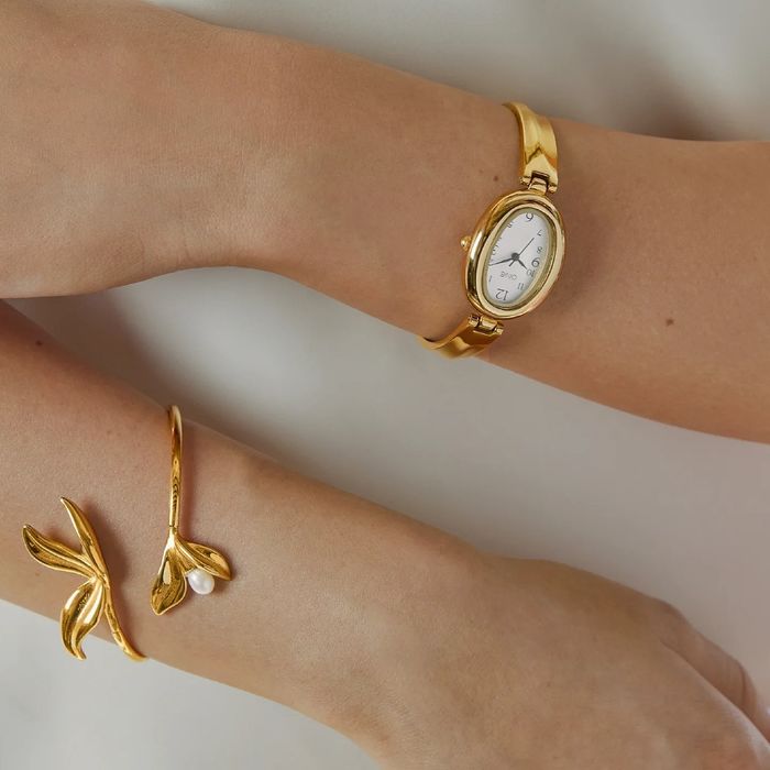 Braços de modelo com uma pulseira e um relógio dourado One de bracelete estilo escrava e caixa oval.