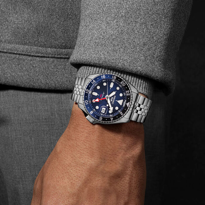 Imagem de pulso masculino com Seiko 5 de bracelete e caixa em aço prateado e mostrador azul.