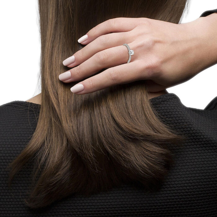 Vista traseira de modelo feminino com um anel prateado com pedras cravadas e um solitário no topo.