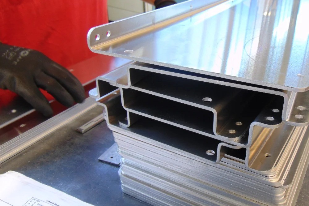 Worker performing sheet metal bending with dimensional control table and stacked stainless steel bent parts