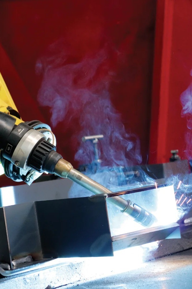 Robotic welding in action with a FANUC robot welding a carbon steel part, showing precision automation in industrial metal fabrication.