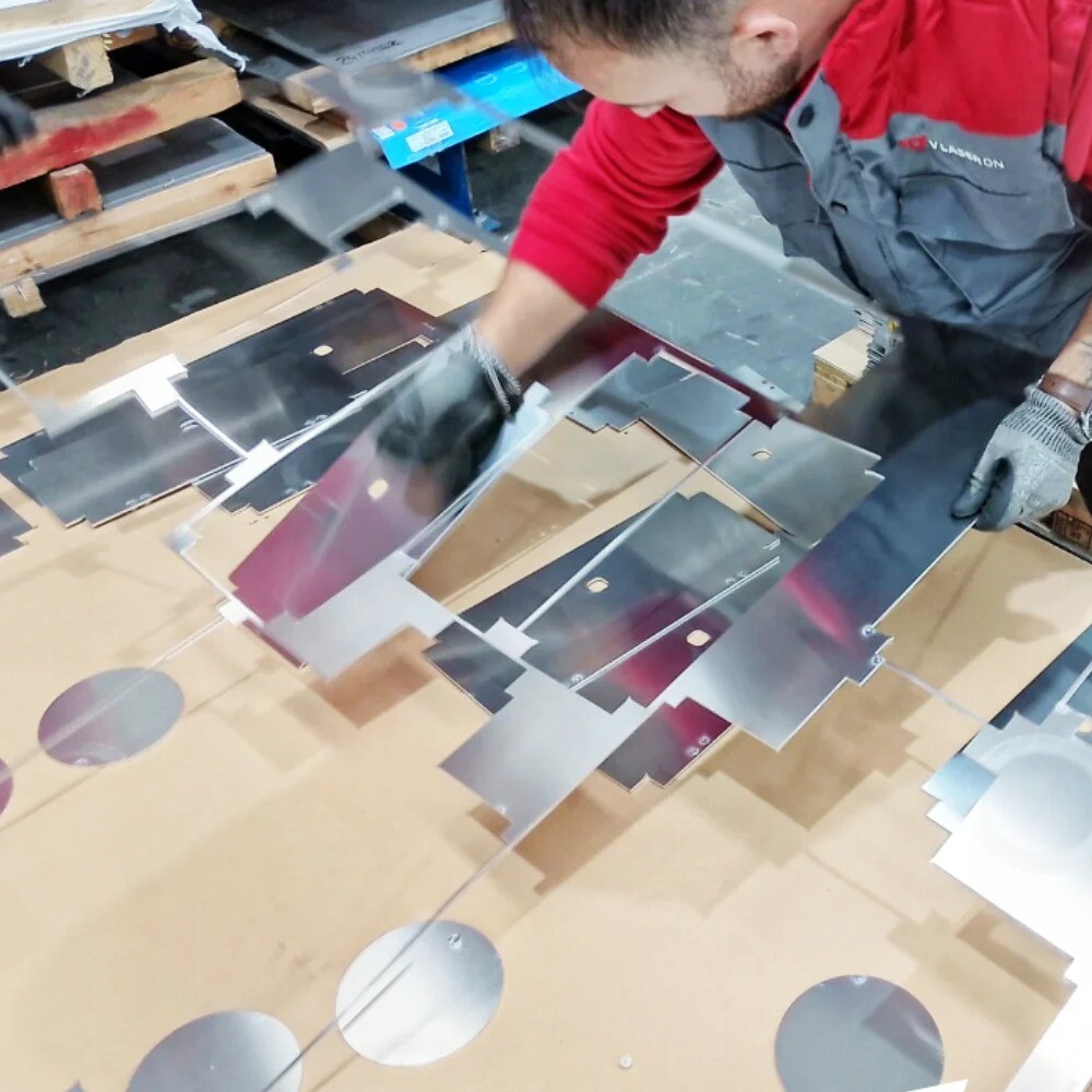 Worker separating laser-cut metal parts from sheet in an industrial facility, showcasing precision sheet metal fabrication