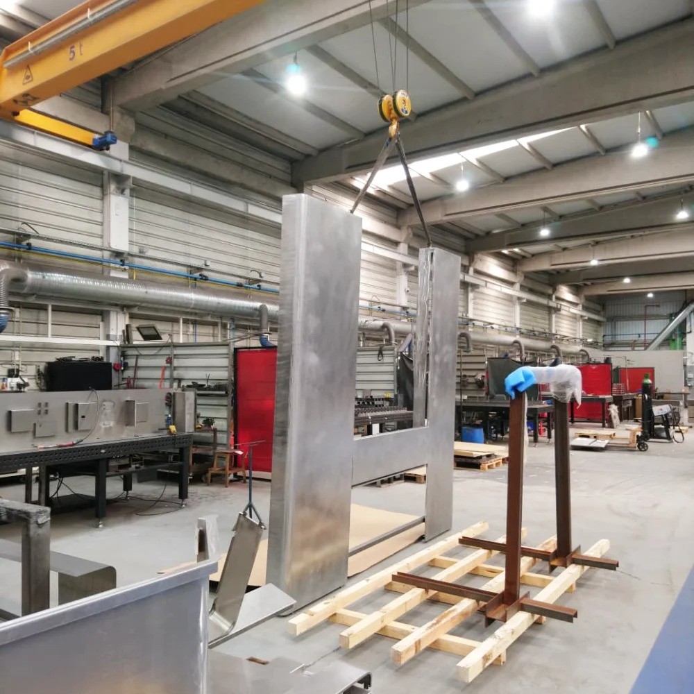 Welded steel structure of a machine casing being lifted by an overhead bridge crane inside the V Laser On welding facility in Porto Portugal, showcasing large-scale industrial welding capabilities