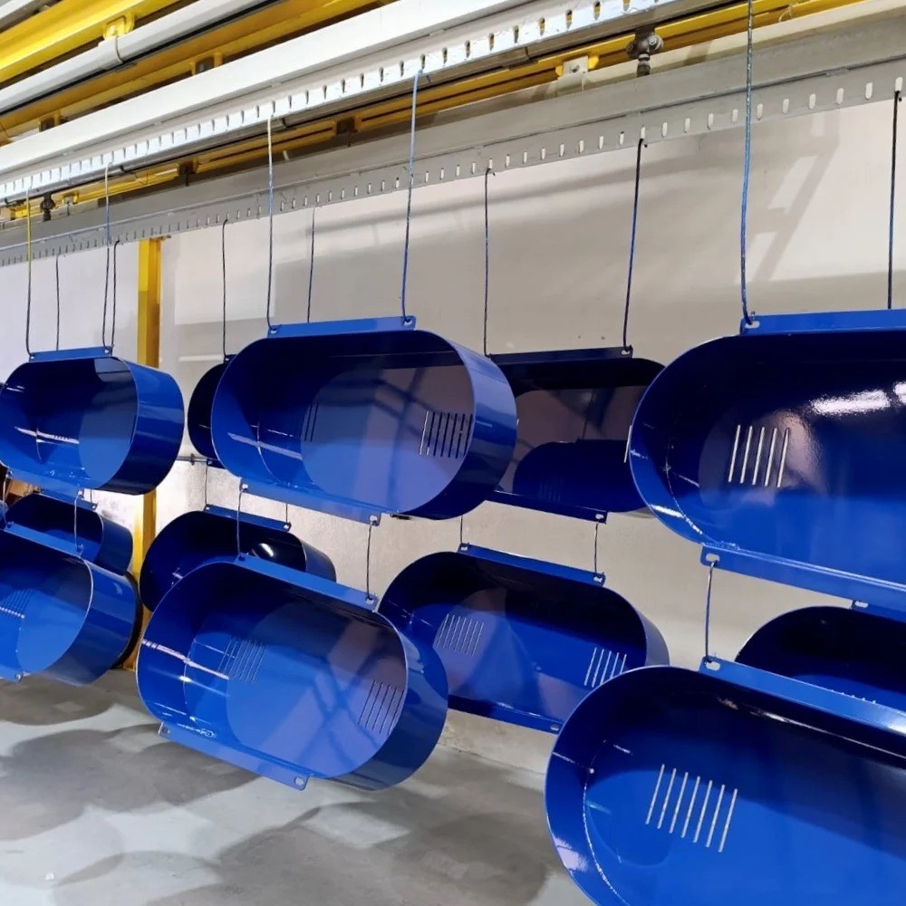 Blue-painted metal assemblies cooling after oven curing, hanging on an overhead rail system at V Laser On workshop in Porto Portugal, showcasing high-quality electrostatic powder coating for industrial components