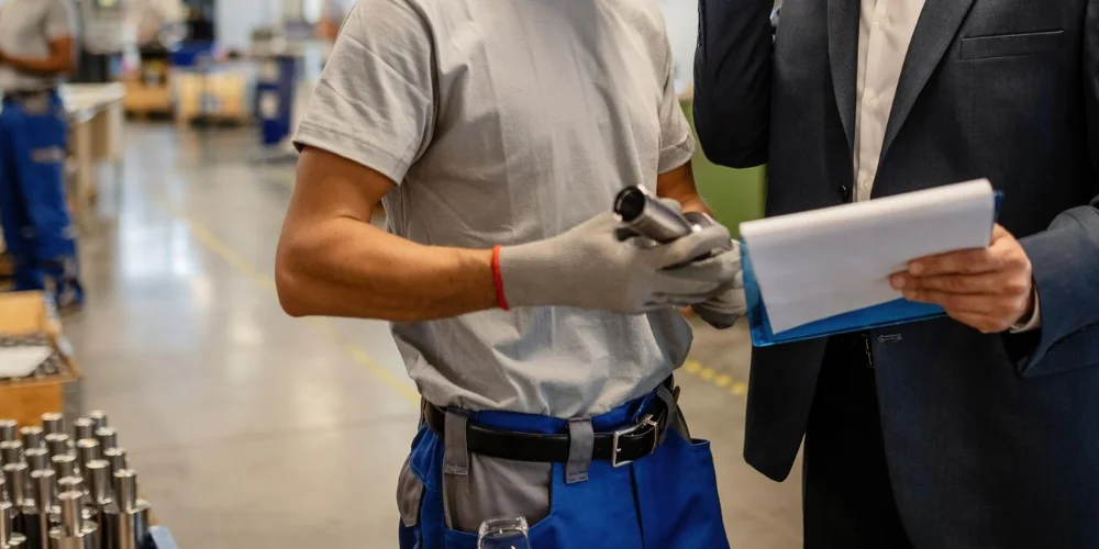 Cost estimation manager in a suit reviewing accounts with a factory operator on the workshop floor at V Laser On in Porto Portugal, illustrating industrial project planning and coordination
