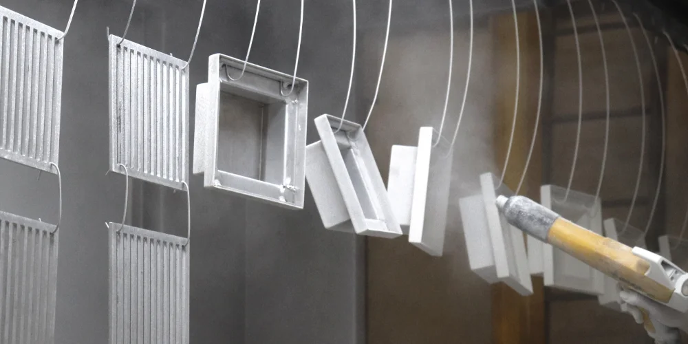 Worker applying white electrostatic powder coating with spray gun on metal components at V Laser On painting line in Porto Portugal, demonstrating industrial powder coating process