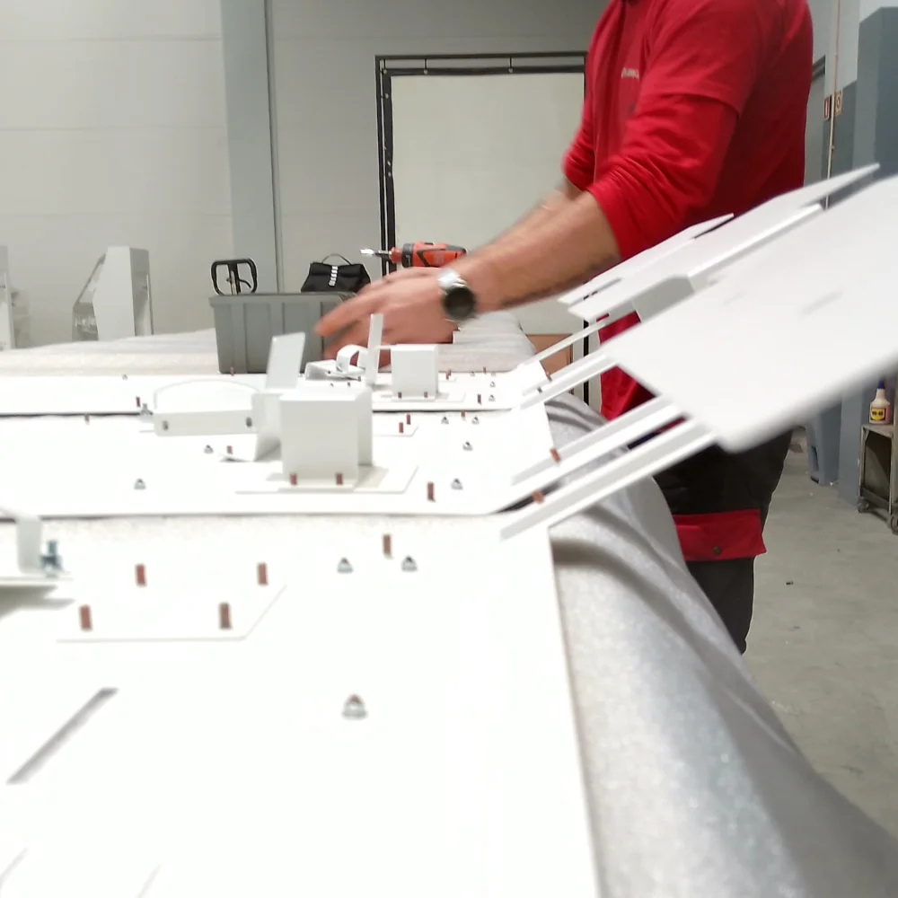 Sub-assemblies of metal components on a workbench with a worker assembling them in the background at V Laser On in Porto Portugal, showcasing precision industrial assembly workflow
