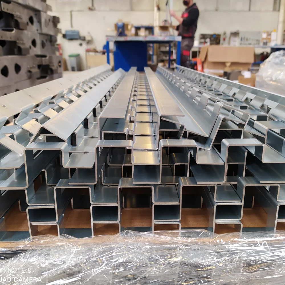 Bent metal profiles stacked in the workshop with a V Laser On team member visible in the background in Porto, Portugal, illustrating precision sheet metal bending and industrial fabrication