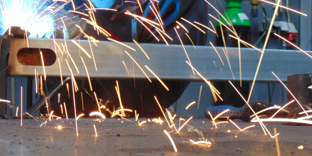 Close-up of welding sparks flying from a carbon steel component during manual welding at V Laser On workshop in Porto Portugal, showcasing industrial metal fabrication